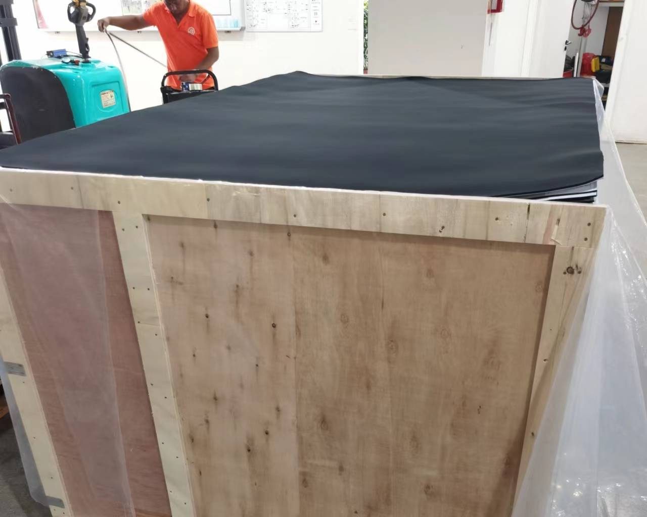 Neoprene sheets packed into an export crate, wrapped in film on a pallet with an operator moving it by stacker truck